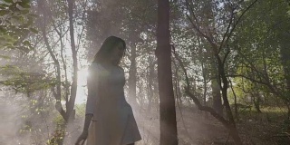 美丽的年轻新娘穿着简单的白色礼服在公园里的秋叶和慢镜头中的烟雾中玩耍