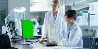 坐在办公桌前的亚洲科学家正在向高级工程师咨询绿色屏幕的个人电脑。在计算机科学研究实验室的机械臂模型。