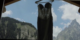 礼服挂在窗前，剪影映衬在天空群山的背景近处。性感的内衣优雅的婚礼晚上打开礼服绣在衣架上与两只鸟飞在云。欧洲旅游婚礼