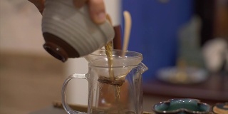 用手将沏好的绿茶倒入有滤纸的玻璃茶壶中