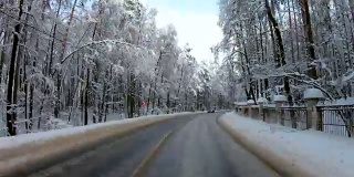 汽车行驶在冰雪覆盖的公路上，沿途是冬日的森林
