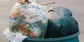 在汽车和摩托车行驶的繁忙街道上，塞满塑料袋、剩饭剩菜和其他垃圾的垃圾桶