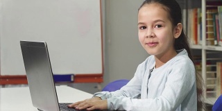 快乐美丽的亚洲小女孩微笑，同时使用笔记本电脑