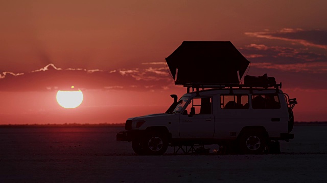 在Makgadikgadi pan，博茨瓦纳，一辆4x4旅游车辆的延时拍摄和日落