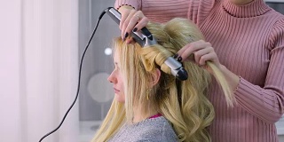 美容院的理发师为客户做头发。金发长头发的病人