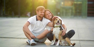 户外肖像相爱的夫妇享受夏天日落与比格尔狗坐在城市广场