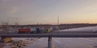 在冬季的景色中，汽油车在冰冻的河流上的桥上行驶