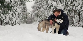 一名男子在森林里拥抱他的西伯利亚哈士奇。在雪的背景树。眼里是骄傲和幸福。带狗散步