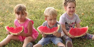 三个孩子在绿色夏季公园吃西瓜