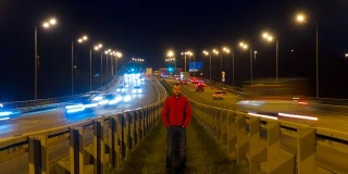 一个人站在公路上。随着时间的推移，高速公路的交通使汽车在夜间变得模糊不清。汽车在桥上行驶的晚上时间流逝。4 k UHD