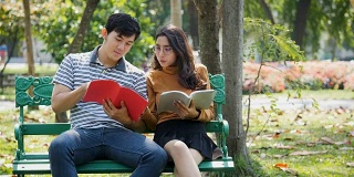 两个亚洲年轻的大学生或情侣正在户外公园的长椅上看书