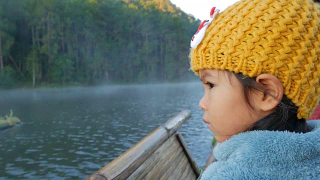 一个可爱的小女孩在竹筏上通过雾漂浮在湖面上在早上，在泰国Mae Hong Son