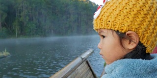 一个可爱的小女孩在竹筏上通过雾漂浮在湖面上在早上，在泰国Mae Hong Son