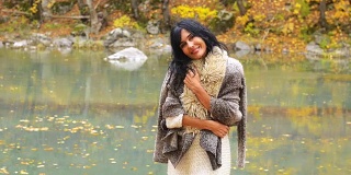 美丽的年轻黑发女子站在河边，在秋天的气氛和忧郁的笑声