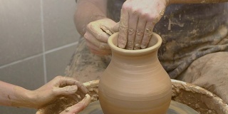 两只手交织在一起，在陶工转盘上形成一个陶罐。
