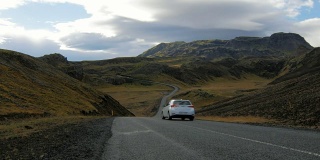 在多云的天气里，白色的汽车在风景如画的冰岛山脉之间的公路上行驶