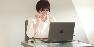 办公室里电脑屏幕后面的女人。商务风格的服装，和电脑一起工作的眼镜。看着眼镜，微笑着