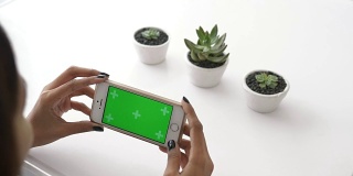 女人的手一边用智能手机，绿色的屏幕一边试图在白色的桌子上捕捉仙人掌，特写-股票视频