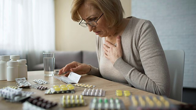 悲伤的女人看着满桌的药片，叹气，年老的疾病，上瘾