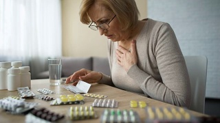 悲伤的女人看着满桌的药片，叹气，年老的疾病，上瘾视频素材模板下载