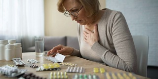 悲伤的女人看着满桌的药片，叹气，年老的疾病，上瘾