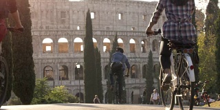 三个年轻的朋友游客骑自行车在colle oppio公园前的罗马斗牛场在路上与树木日落在罗马慢镜头
