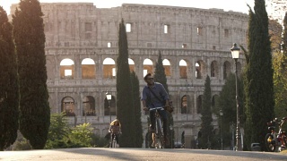 三个年轻的朋友游客骑自行车在colle oppio公园前的罗马斗牛场在路上与树木日落在罗马慢镜头视频素材模板下载