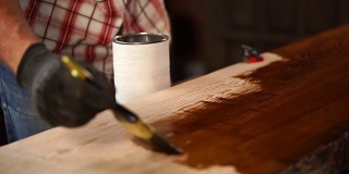 男子正在把棕色的漆涂在木板表面，油漆铺子