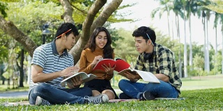 一群年轻的大学生坐在公园外面的草地上看书
