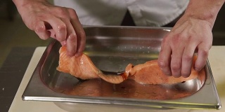 一个厨师的手的特写镜头，一个男人正在烹饪一块鳟鱼在一家餐馆