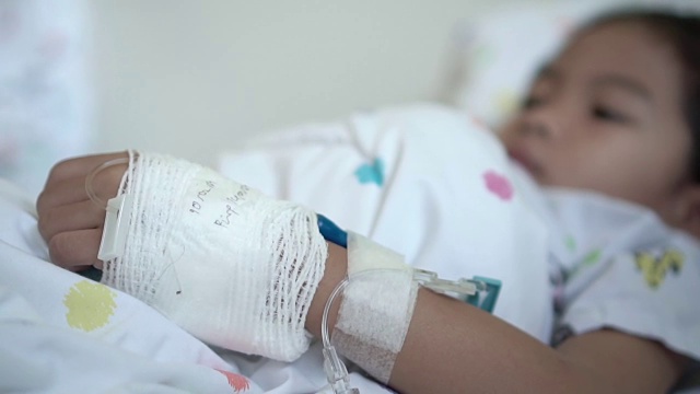 生病的亚洲女孩包扎手的特写，而躺在医院的床上。治疗室实时拍摄。