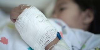 放大生病的亚洲女孩的手绷带，而躺在床上在医院。治疗室实时拍摄。