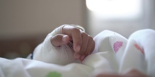 生病的亚洲女孩包扎手的特写，而躺在医院的床上。治疗室实时拍摄。