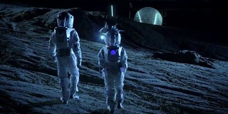 下面是两名宇航员穿着太空服行走在外星星球上仰望天空的照片。在背景基地与球型圆顶。其他世界殖民和太空旅行的概念。