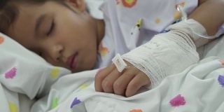 当生病的亚洲女孩在医院的床上睡觉时，她的手被包扎得紧紧的。治疗室实时拍摄，慢动作拍摄。