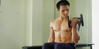 年轻的亚洲健美者在健身房用哑铃练习，健康和生活方式的概念