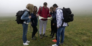 一群迷路的年轻游客徒步寻找方向，通过雾在山顶上阅读地图