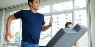 年轻的健身男子在跑步机上跑步，在健身房和女教练锻炼，健康的生活方式和有氧训练的概念