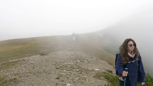 徒步旅行者十几岁的女人走在探索山景点的道路与雾与游客的背景