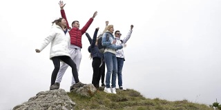 快乐的一群朋友爬上山顶，跳跃，举起手臂，享受他们的成就的成功