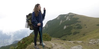 年轻的徒步女子背着背包，在石质的山坡上爬上山顶
