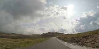 Pov的乡村道路与丘陵和多云的天空在背景中看到从驾驶车辆旅行