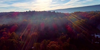 这是宾夕法尼亚州波科诺斯阿巴拉契亚山脉森林上空的雾的鸟瞰图，在秋叶季节的清晨。对着太阳拍摄，镜头光晕和日光。