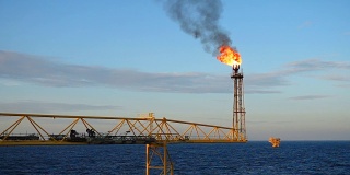 慢动作的气体火炬燃烧在海上的油气平台上，在海与蓝天为油气行业的概念。