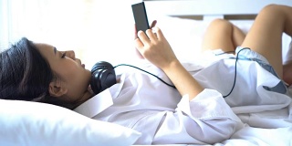 特写:美丽的女人躺在床上，打着哈欠与智能手机