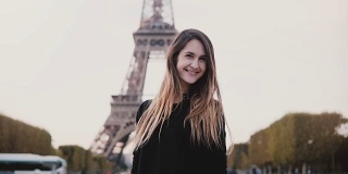 年轻快乐的女子站在法国巴黎埃菲尔铁塔附近，对着镜头微笑，并发送飞吻