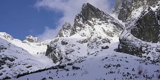 在寒冷的阳光明媚的天气里，滑雪游览覆盖在雪中的岩石山脉景观