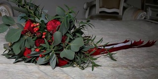 床上放着漂亮的婚礼花束，是用丝带裹着的红玫瑰和牡丹。特写镜头。