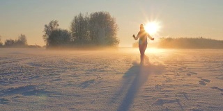 女人在冬天跑过田野，踢着雪在日落时飞着雪花