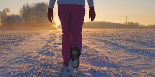 一名女子在冬日里的日落时分走在白雪覆盖的田野上